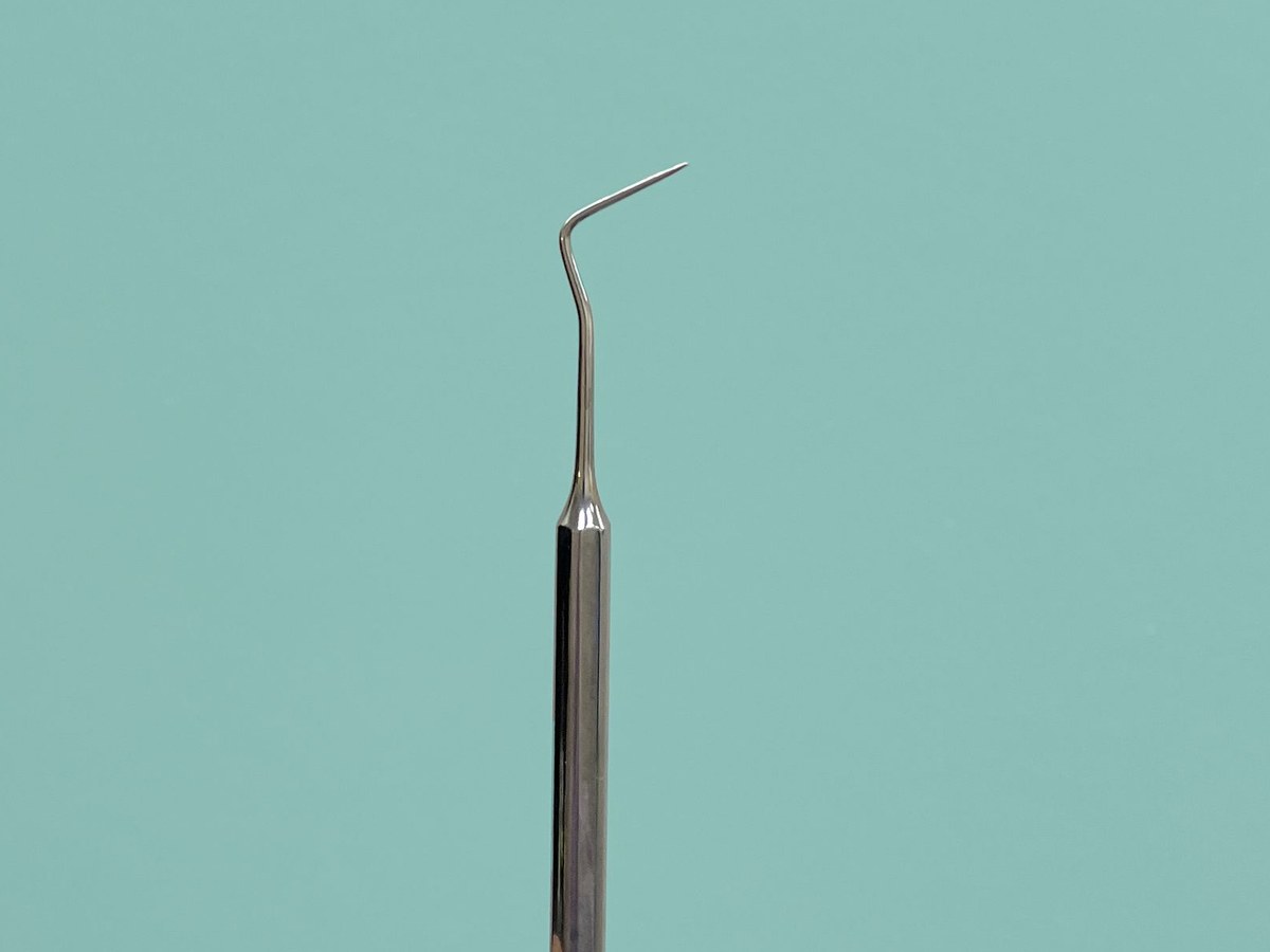 Dental scaler against a plain turquoise background