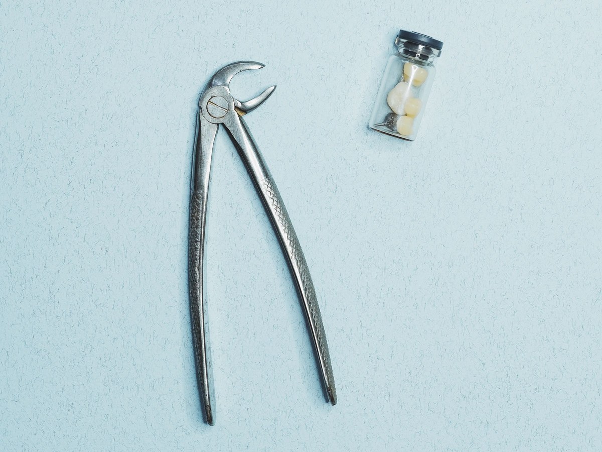 Dental extraction forceps beside a small vial of extracted teeth
